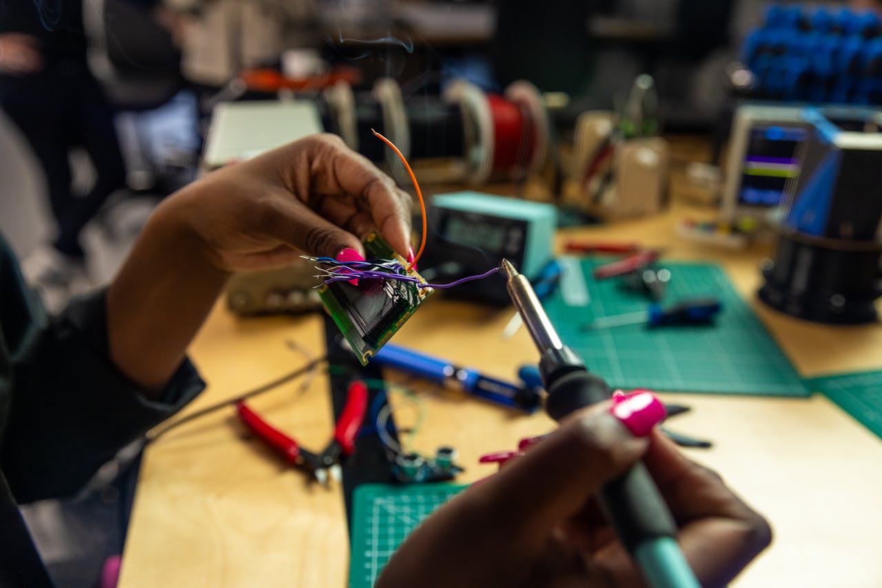 Hands of a female worker soldering an electronic component in a tech workshop setting.